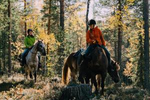 two people are riding horses in the woods at Lucky Ranch cabin 4 in Pyhätunturi