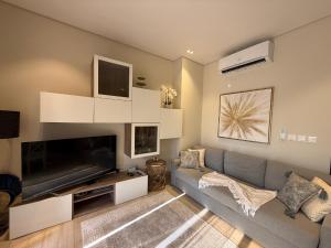 a living room with a gray couch and a flat screen tv at Sunset Hawana in Salalah