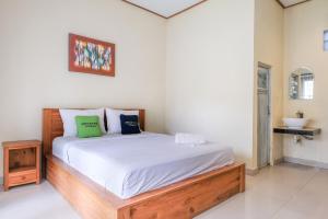 a bedroom with a bed with white sheets and green pillows at Lilis Cempaka Mas Guesthouse in Canggu