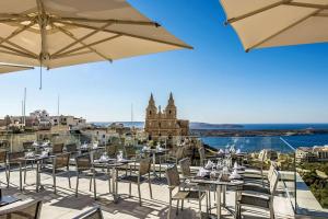 un restaurante con mesas y sombrillas en el balcón en Maritim Antonine Hotel & Spa, en Mellieħa