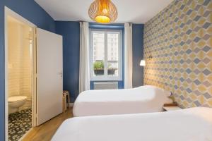 Dos camas en una habitación con paredes azules y una ventana. en Les Toits de Paris, en París