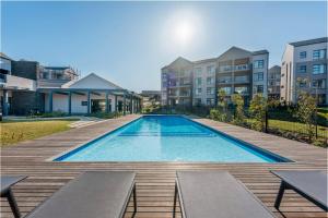 a swimming pool with benches on a wooden deck with buildings at Luxury Spa unit, Private Sauna, Central Ballito in Ballito
