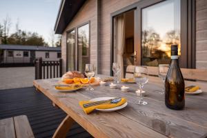 a wooden table with a bottle of wine and glasses at Olive Lodge Benllech in Brynteg