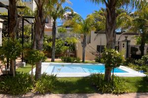 a swimming pool in front of a house with palm trees at At Villa Fig Guest House in Constantia