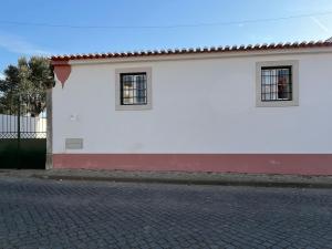 a white building with two windows on a street at Casas do Hastim in Golegã