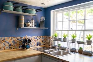 a blue kitchen with a sink and a window at Thyme Cottage in Beccles