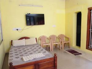 a room with a bed with chairs and a tv on the wall at Nandy Delight Homestay in Kanyakumari
