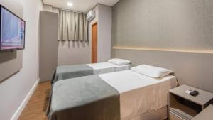 two beds in a small room with a tv at Florida Limeira Hotel in Limeira