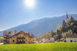 a yellow house in a field with a church at Hotel Tolderhof in San Candido