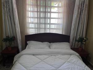 a bed with white sheets and a window with curtains at Golf BnB in Nyahururu