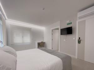 a white bedroom with a large bed and a flat screen tv at 6 de Mayo alojamientos in Almansa