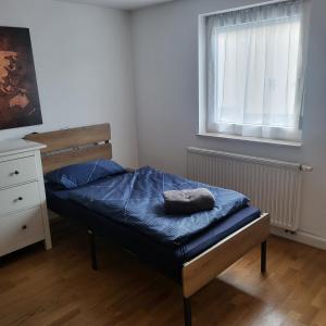 ein kleines Schlafzimmer mit einem Bett mit blauer Bettdecke und einem Fenster in der Unterkunft Bel - Self Check-Inn in Eggenfelden