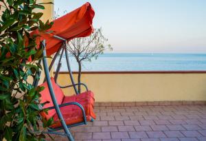 een rode stoel op een patio met uitzicht op de oceaan bij Hotel Nizza in Nizza di Sicilia