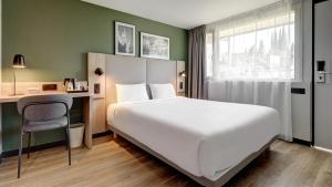 a hotel room with a large white bed and a desk at Campanile NATURE - Compiegne in Compiègne