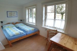 a bedroom with a bed and a table and two windows at Haus am Deich in Utersum