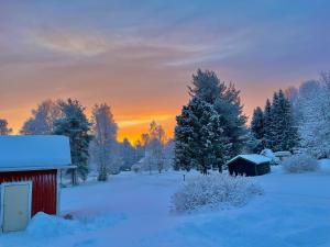 a red barn in a snow covered field with a sunset at The Little Owls Nest in Rovaniemi