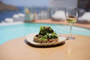 a plate of food and a glass of wine on a table at Infinity Blue Boutique Hotel Astypalaia in Astypalaia