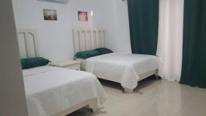 a bedroom with two beds with white sheets and green curtains at Hotel Dieux Internacional in Pedernales