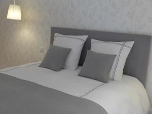 uma cama com lençóis brancos e almofadas cinzentas em Maison de Luciné em Combourg