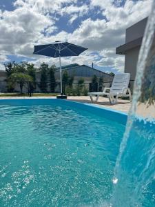 a swimming pool with an umbrella and a white chair and a table and an umbrella at Casa de descanso, completa, para ate 05 pessoas in Pântano Grande +4 photos