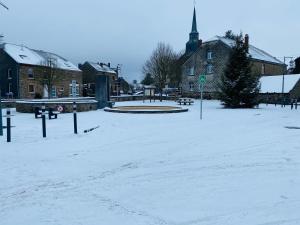 a snow covered street in a town with a church at L Abri douillet in Libin