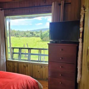 Ein Schlafzimmer mit einem Fernseher auf einer Kommode und einem großen Fenster in der Unterkunft Chiloe Profundo in Chonchi