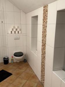 a bathroom with a toilet and a tiled wall at Work & Sleep Am Waldesrand in Vollersode