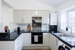 a kitchen with white cabinets and black counter tops at West London Spacious Modern House Garden Driveway in London