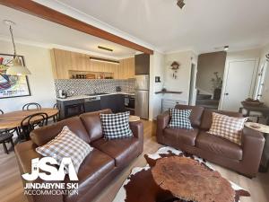 a living room with a brown couch and a kitchen at Lakeside Chalet in Jindabyne +5 photos