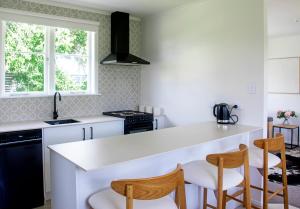 a kitchen with a white counter and wooden chairs at Glenmohr Cottage in Waipu