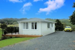 a small white house with a yellow car parked in the driveway at Glenmohr Cottage in Waipu
