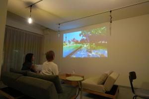 two women sitting in a living room watching a movie on a screen at TomaReno Beppu-Kitahama in Beppu