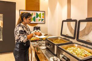 a woman is preparing food in a buffet at Treebo Premium Landmark Prayagraj in Prayagraj