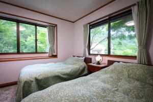 two beds in a bedroom with two windows at Bessou Konjakuan in Yufu