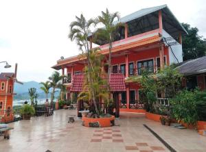 a red building with palm trees in front of it at Phonevichith Riverside Hotel Houayxai in Ban Khonkèo