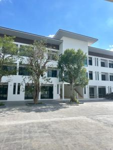 a white building with two trees in front of it at J&P Hotel Sriracha in Ban Laem Chabang