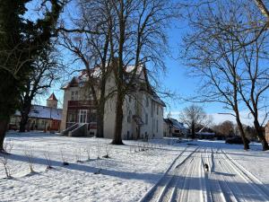 a snow covered street with a house and trees at Ferienwohnung Domaene Kermen in Kermen