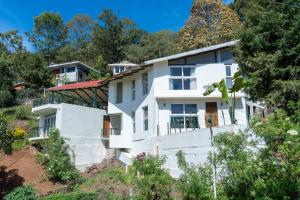 a white house on a hill with trees at SaffronStays Valleyfall in Kotagiri