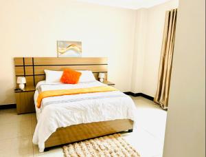 a bedroom with a bed with an orange pillow on it at Asamez Apartments in Lilongwe