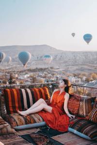 a woman in a red dress sitting on a couch with hot air balloons at Virtus Cappadocia Hotel Göreme in Göreme