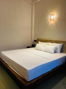 a bed with white sheets and a light on the wall at Ancy Villa in Dickwella