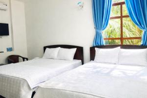 two beds in a room with blue curtains and a window at Green Ville Hotel Đồng Nai in Xa Dau Giay