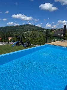 a large blue swimming pool with a playground at Apartament Świerkowa Osada in Istebna