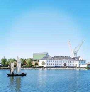 a sail boat in the water with a building and cranes at TheGilgahouse Gardenroom in Nakskov