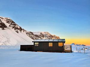 a cabin in the snow with mountains in the background at Aurora Cabin and Private Jacuzzi in Hvolsvöllur
