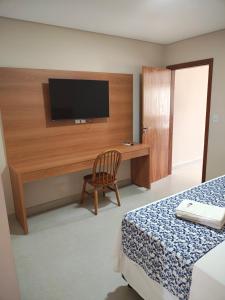 a bedroom with a desk with a television on a wall at Valparaiso Hotel in Cruz das Almas