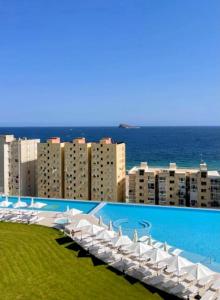 a row of white umbrellas and chairs next to a city at Sunset Cliffs Luxury Apartment Benidorm in Benidorm