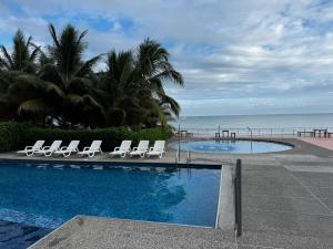 a swimming pool with lounge chairs and the ocean at Departamento frente al mar - Resort Playa Azul in Tonsupa