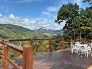 a wooden deck with white tables and chairs on a mountain at Pousada Sítio Rústicu's in Domingos Martins