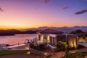 a house on the water with the sunset in the background at Elounda Olivia Luxury Villa Spinalonga View in Elounda